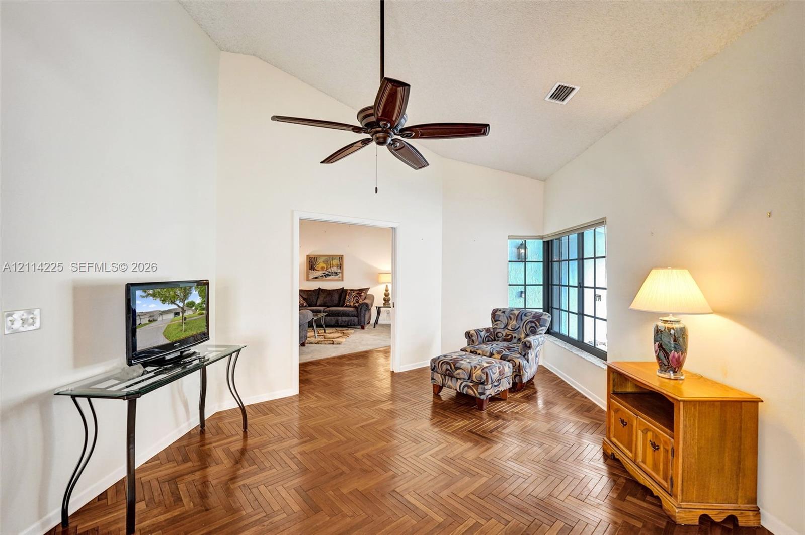 Vaulted ceilings featuring a dark-finish ceiling fan, wood-finish flooring in a herringbone pattern, and multi-pane windows