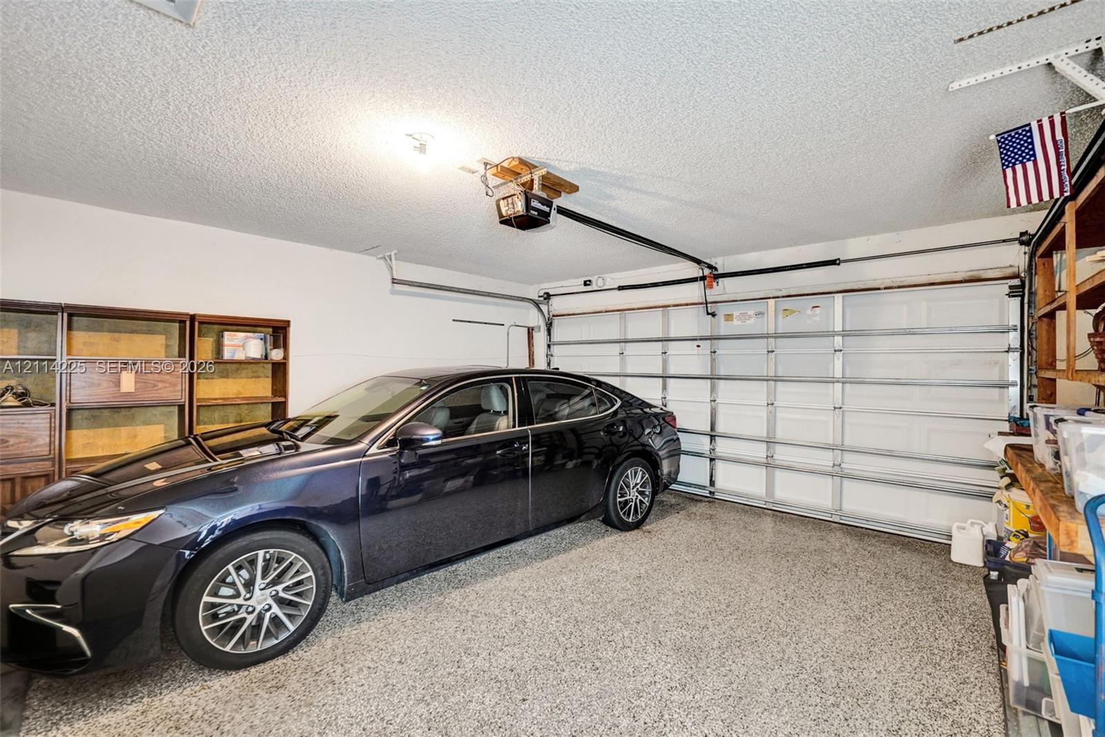 Attached garage featuring epoxy-coated flooring, a motorized garage door opener, and built-in shelving units