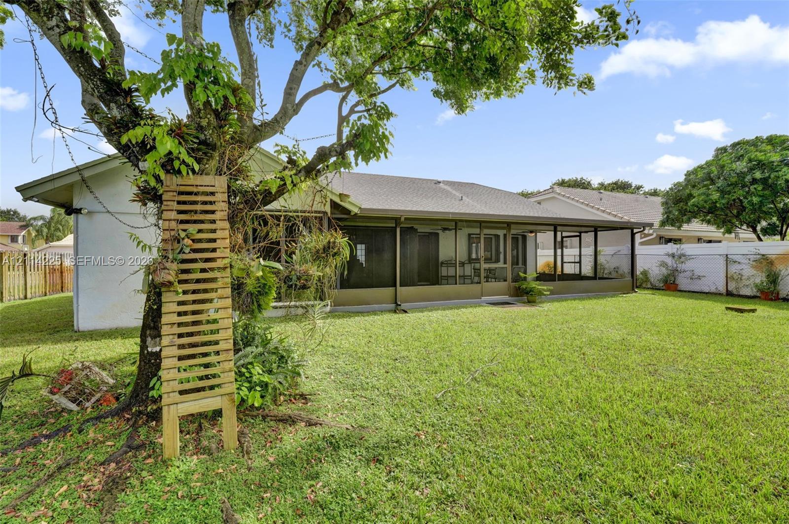 Backyard featuring a grass lawn, screened-in porch, mature tree, and perimeter fencing