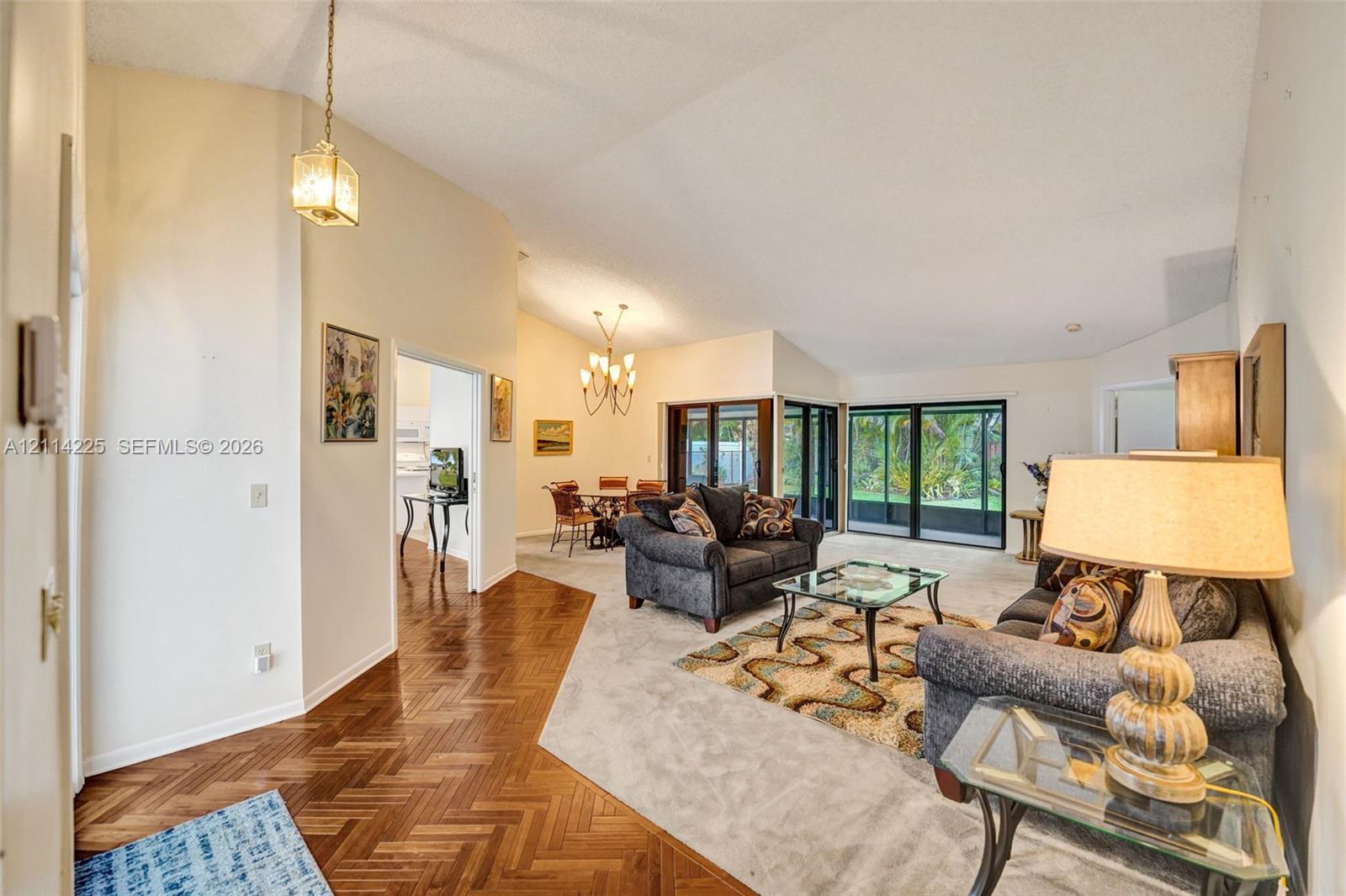 Vaulted ceilings, herringbone-patterned wood flooring, multi-pane sliding glass doors, and dual decorative chandeliers