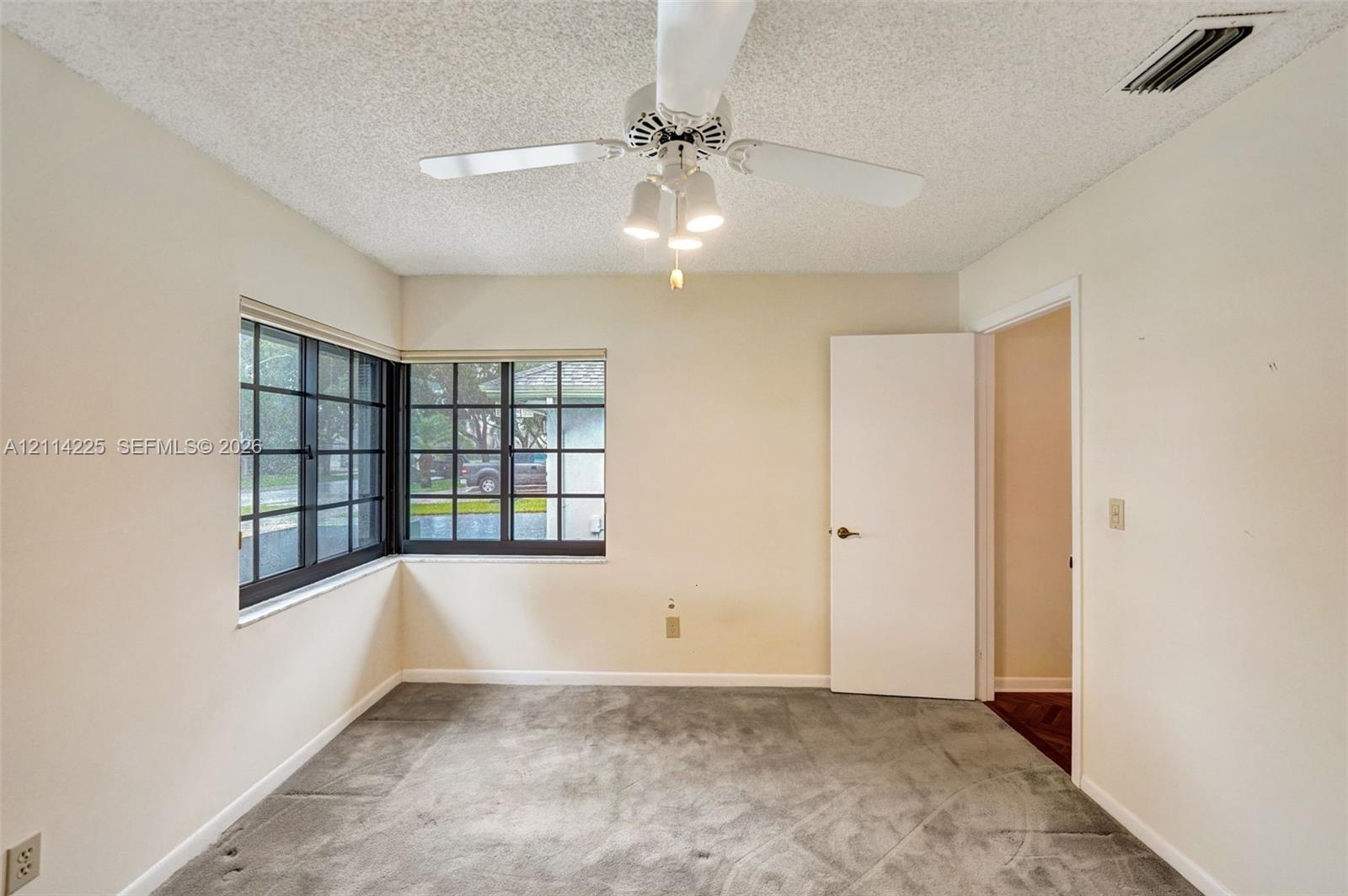 Corner windows with dark-finish frames, neutral wall finishes, and a central ceiling fan with integrated lighting
