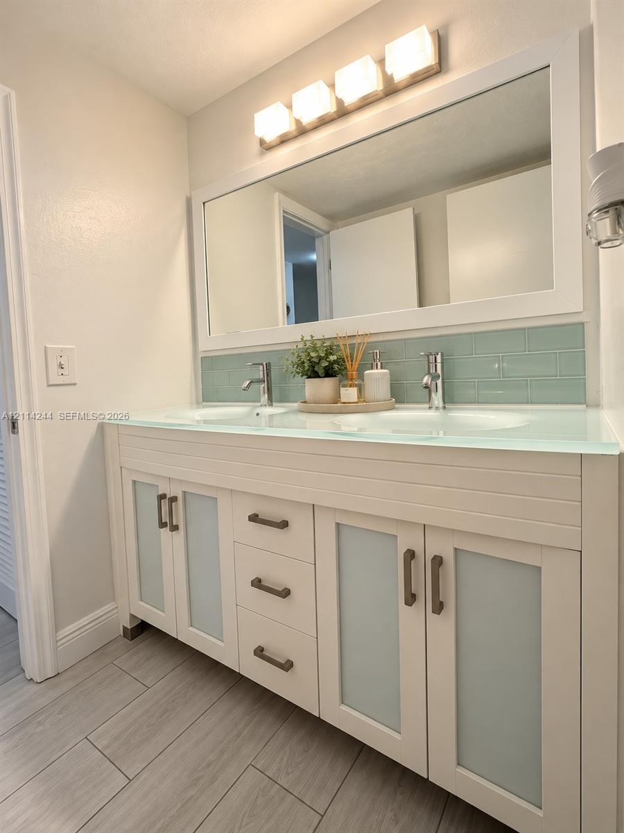 Double vanity featuring frosted glass cabinet doors, integrated glass countertop with dual sinks and light blue subway tile backsplash.