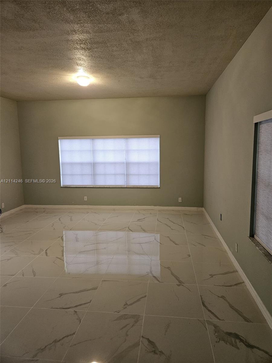 Interior room featuring large-format tile flooring with a veined pattern, neutral-toned wall paint, and windows with integrated blinds Interior room featuring large-format tile flooring with a veined pattern, neutral-toned wall paint, and windows with integrated blinds
