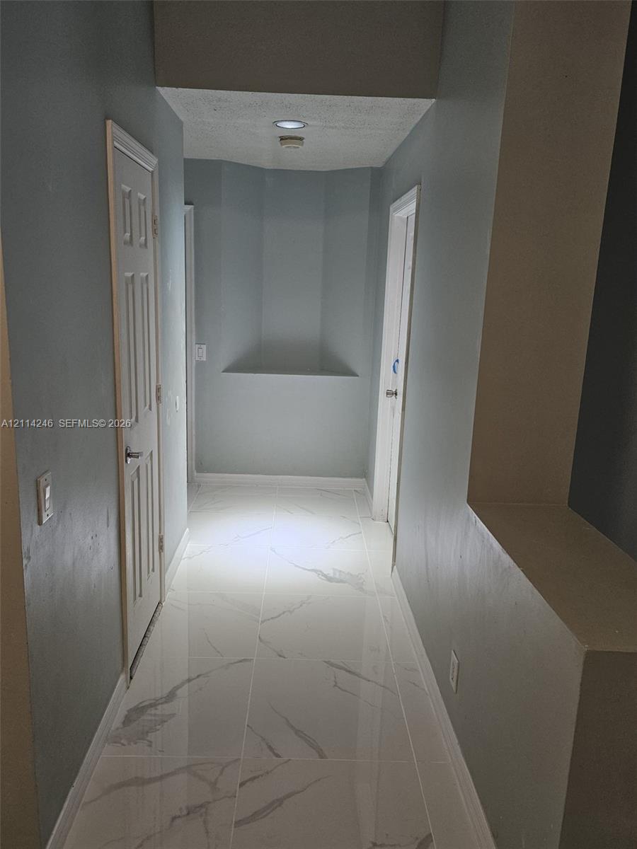 Hallway featuring large-format tile flooring with a veined finish, recessed wall niches, and paneled interior doors Hallway featuring large-format tile flooring with a veined finish, recessed wall niches, and paneled interior doors