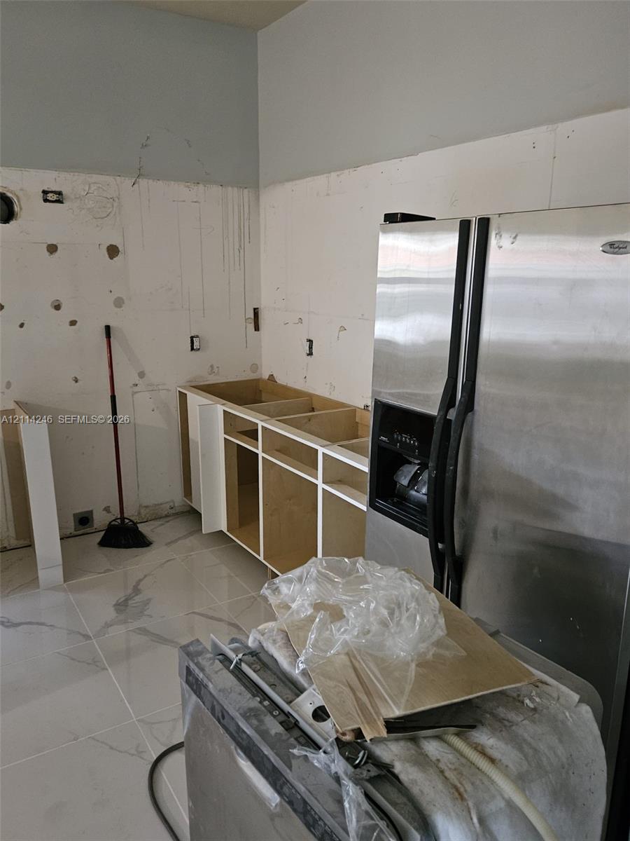 Large-format tile flooring, unfinished cabinetry, and a side-by-side stainless steel refrigerator Large-format tile flooring, unfinished cabinetry, and a side-by-side stainless steel refrigerator