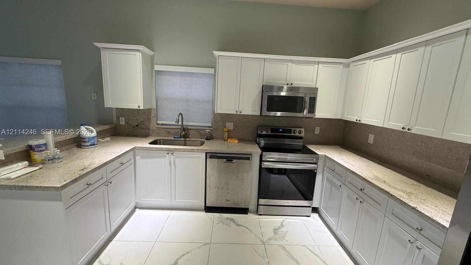 Kitchen featuring white shaker-style cabinetry, stone-finish countertops, stainless steel appliances, an undermount sink, and large-format tile flooring