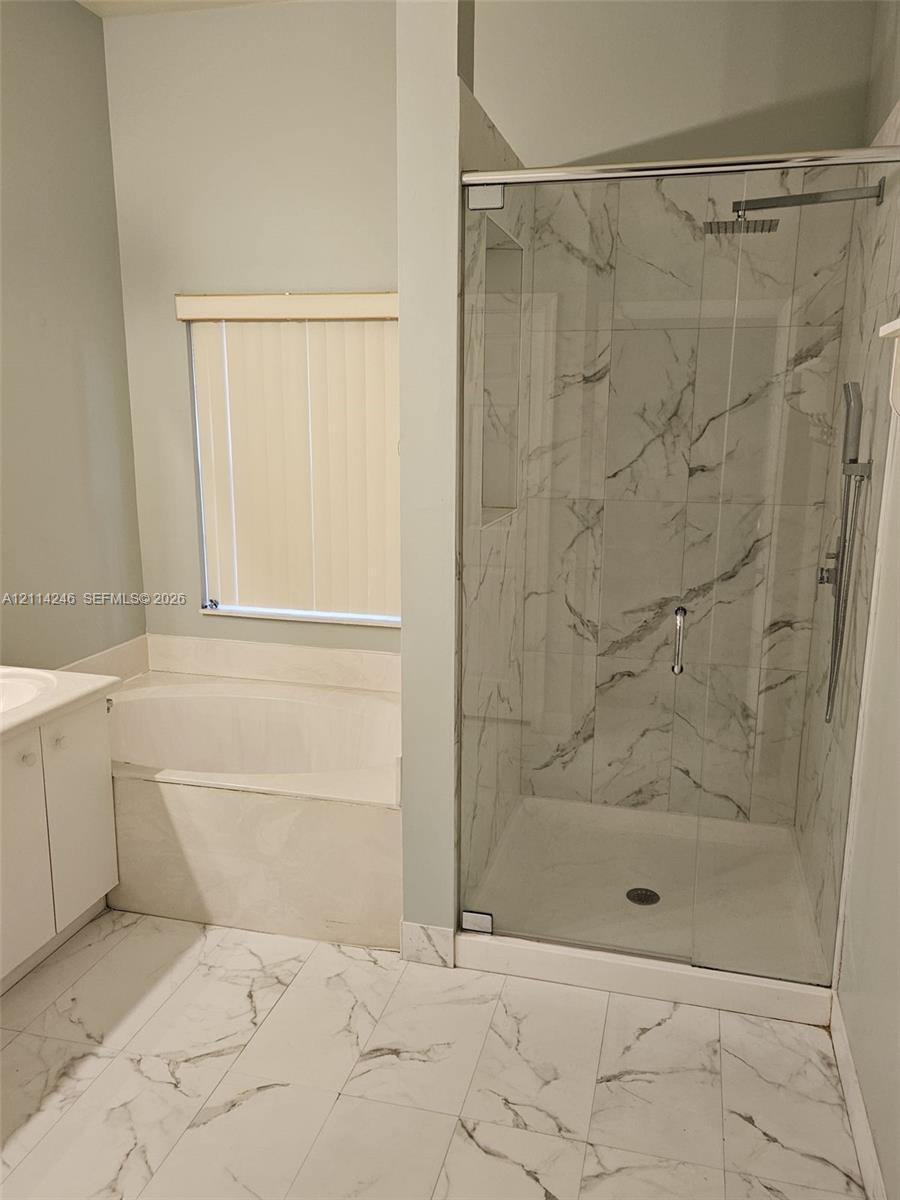 Walk-in shower with stone-finish tile surround, ceiling-mounted rainfall shower head, glass enclosure, built-in soaking tub, and large-format tile flooring