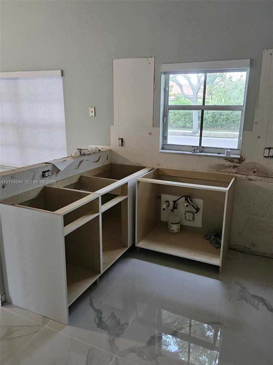 Unfinished kitchen cabinetry featuring white melamine frames and large-format polished tile flooring Unfinished kitchen cabinetry featuring white melamine frames and large-format polished tile flooring