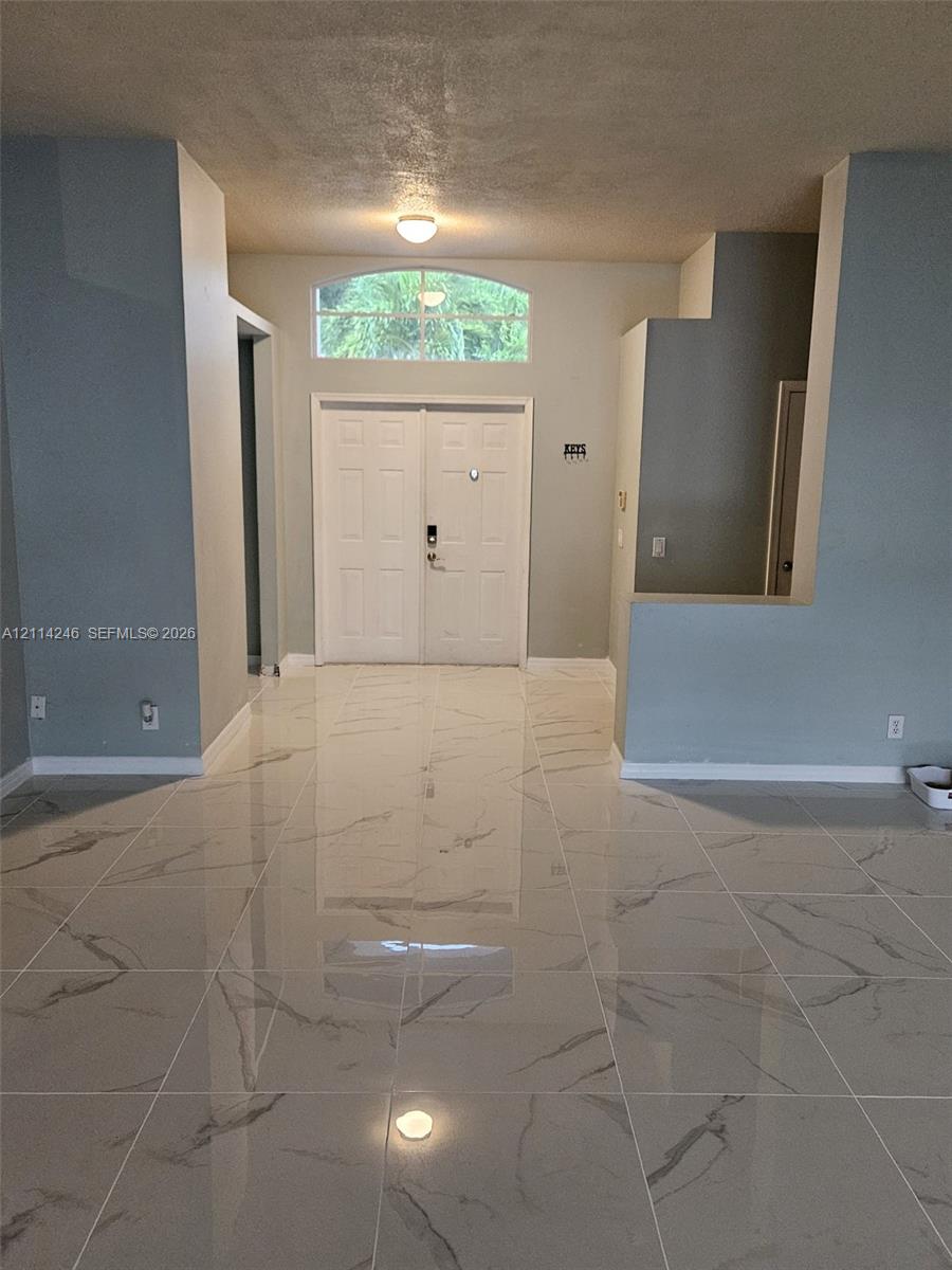 Entryway featuring large-format tile flooring with a neutral veined pattern, double front doors, and a semi-circular transom window Entryway featuring large-format tile flooring with a neutral veined pattern, double front doors, and a semi-circular transom window