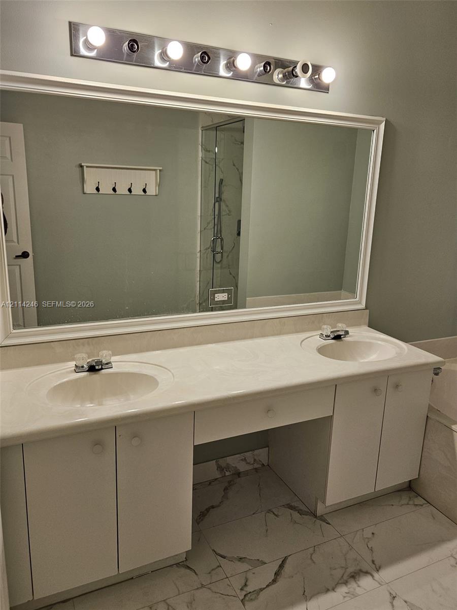 Dual-sink vanity with white cabinetry, integrated stone-finish countertop, full-width mirror, and multi-bulb vanity lighting, accented by large-format floor tiling