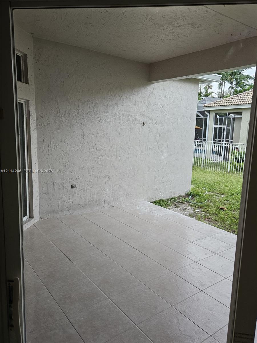 Covered concrete patio featuring large-format ceramic floor tiles, textured stucco walls, and an open entryway to the exterior grounds Covered concrete patio featuring large-format ceramic floor tiles, textured stucco walls, and an open entryway to the exterior grounds