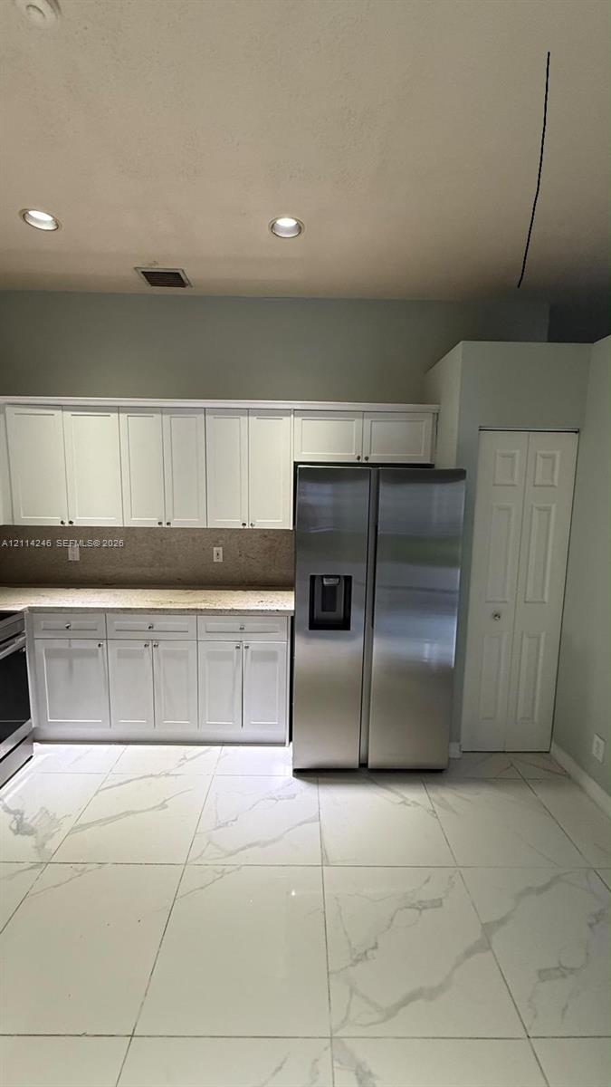 Kitchen featuring white cabinetry, stone-surface countertops, large-format tile flooring, stainless steel side-by-side refrigerator, and recessed ceiling lighting