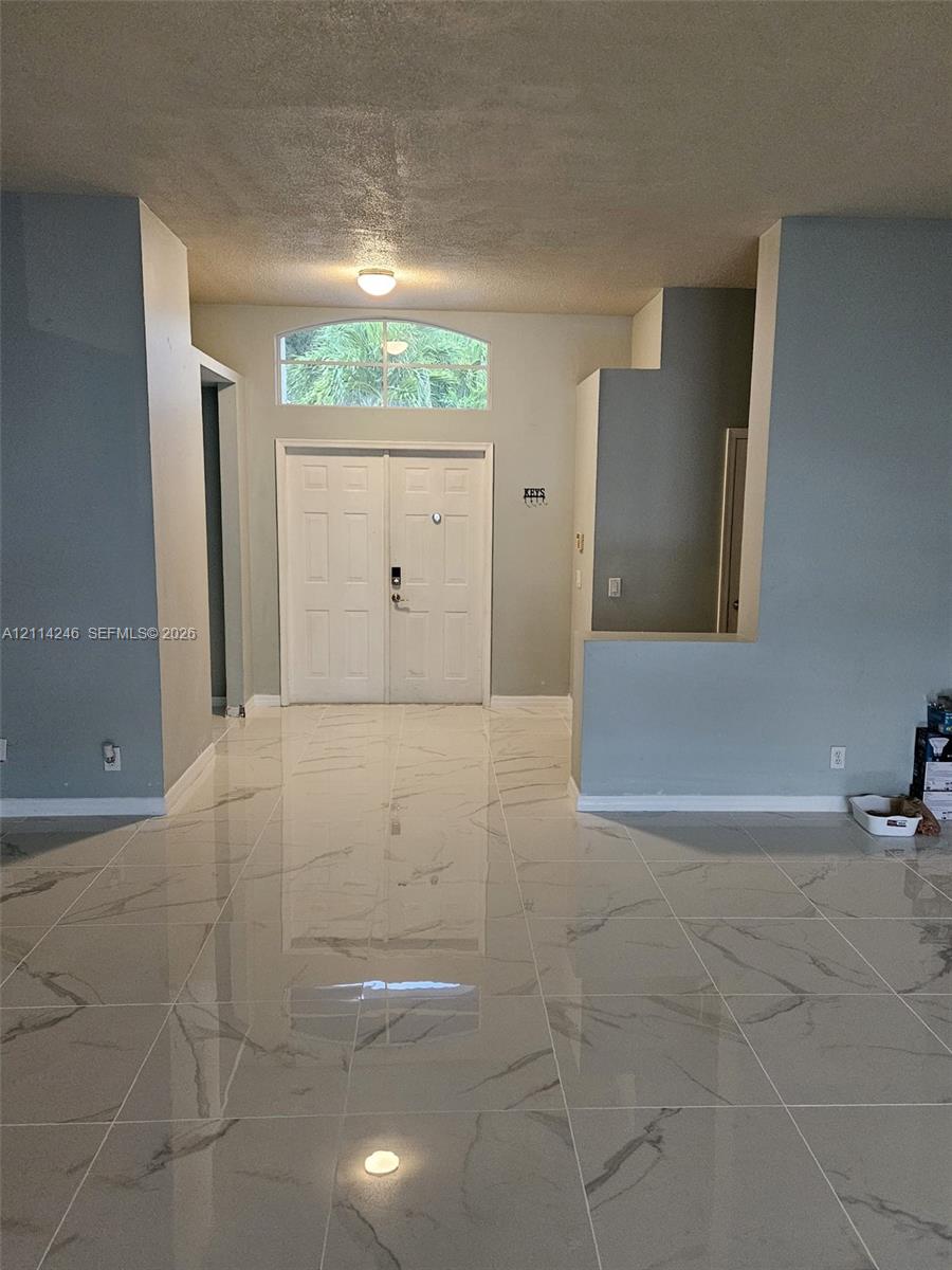 Double entry doors featuring a decorative arched transom window, finished with high-gloss large-format tile flooring and neutral-toned wall paint