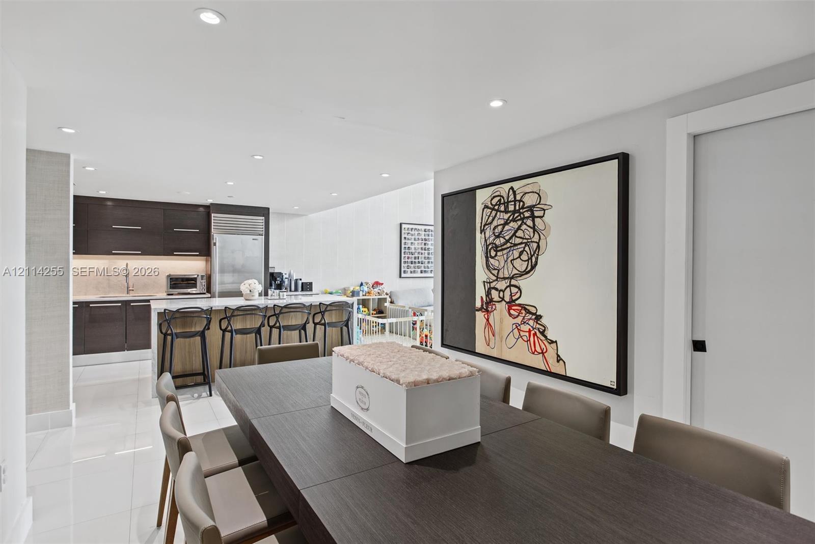 Open-concept kitchen featuring high-gloss dark cabinetry, integrated refrigerator, stone countertops, and recessed lighting throughout