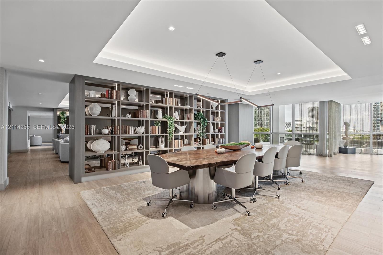 Open-concept space featuring wood-finish flooring, a tray ceiling with recessed lighting, floor-to-ceiling windows, and custom floor-to-ceiling built-in shelving