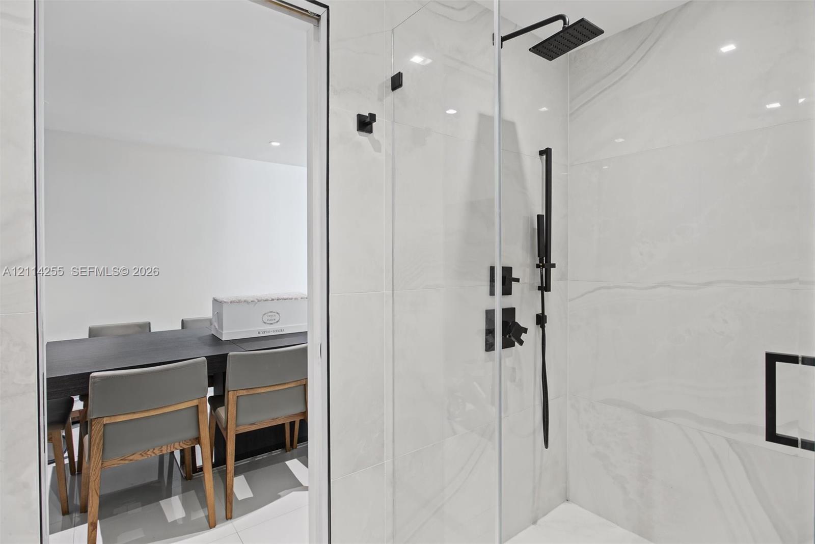 Walk-in shower featuring large-format stone-finish tile, glass enclosure, matte black rainfall showerhead, and matching handheld sprayer