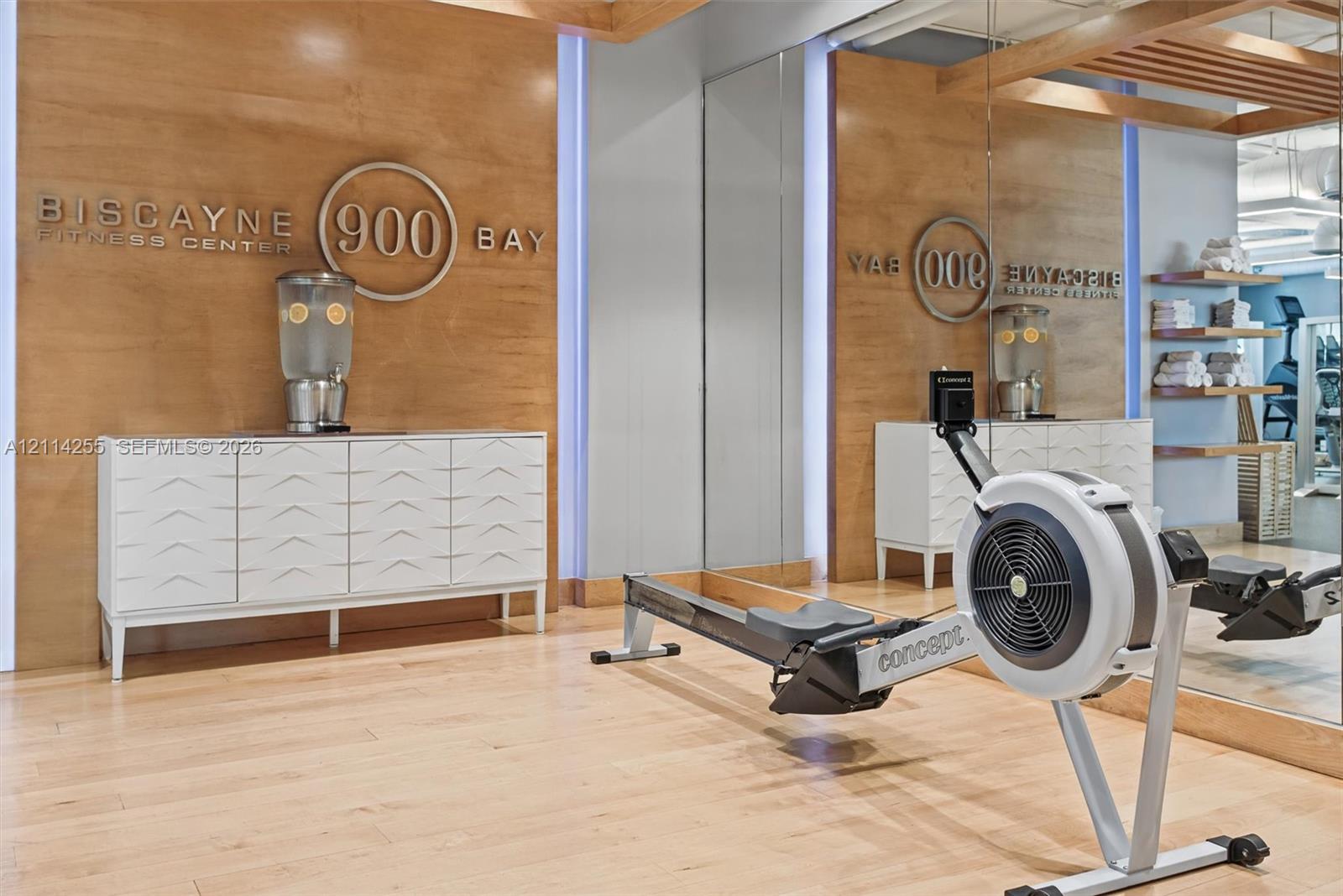 Fitness center featuring wood-panel wall accents, full-height wall mirrors, built-in recessed shelving, and wood-finish flooring