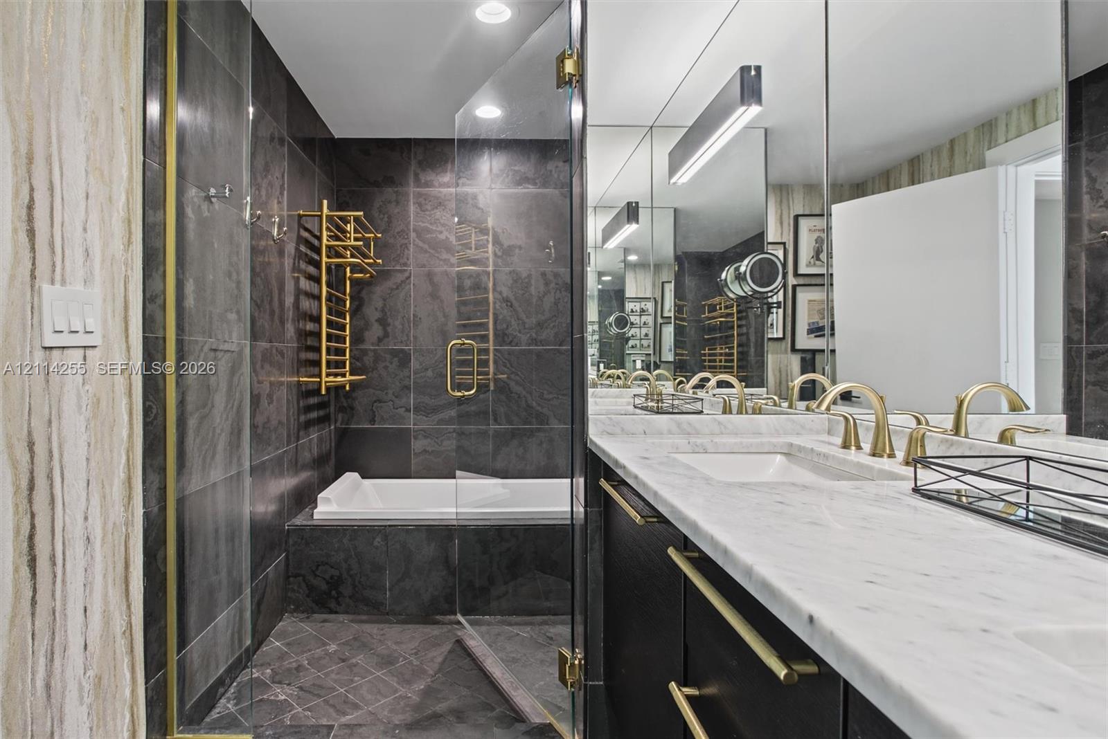 Bathroom featuring a double vanity with stone countertops, dark cabinetry with gold-tone hardware, a glass-enclosed shower, and a built-in tub with wall-mounted gold-tone towel warmer