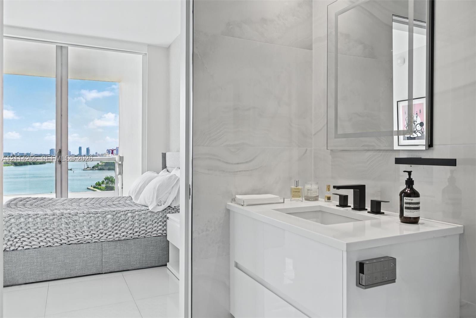Modern floating vanity with a solid-surface countertop, rectangular basin, and matte black faucet, featuring wall-to-wall large-format porcelain tile, a backlit mirror, and floor-to-ceiling glass sliding doors