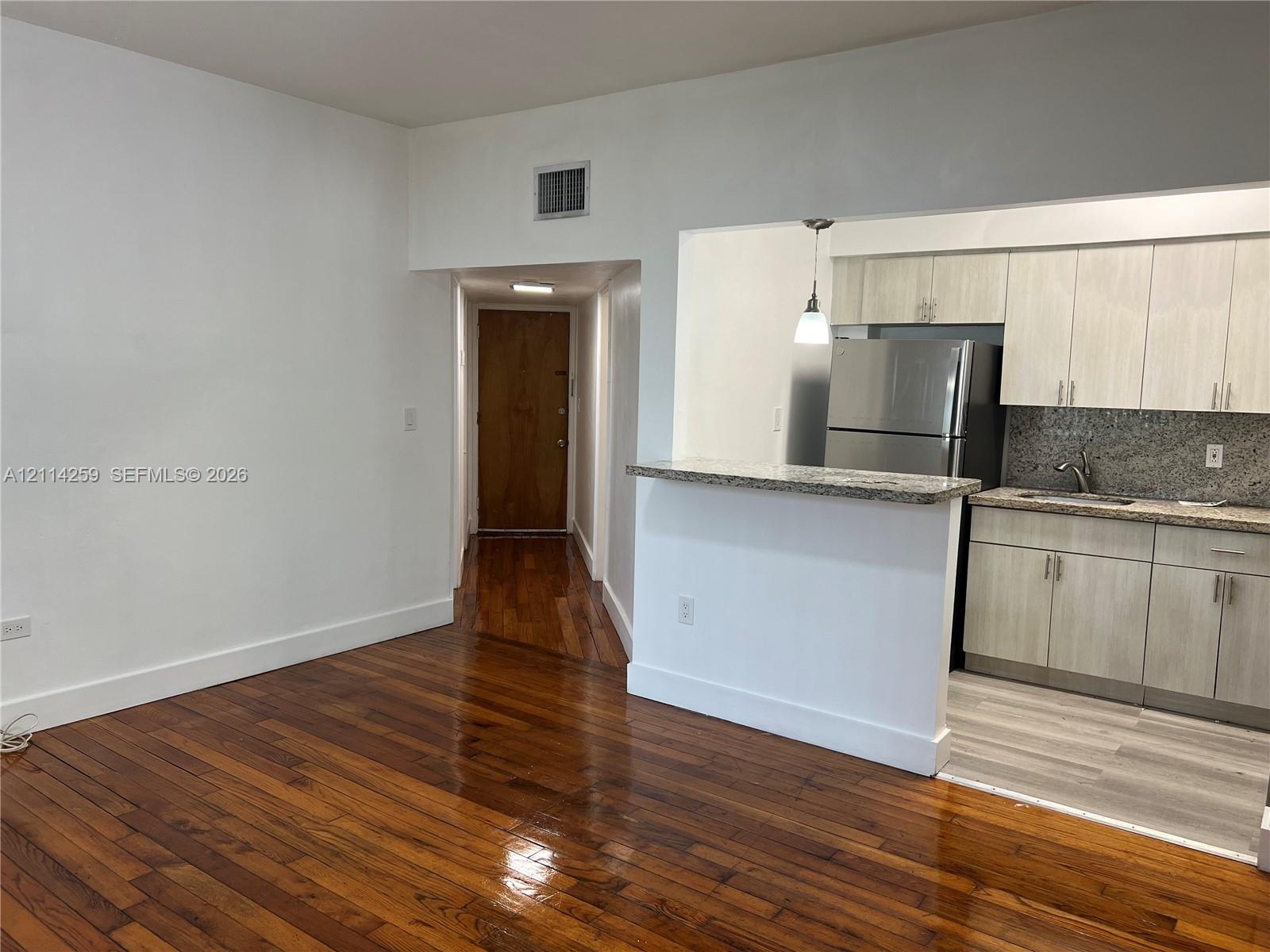 Hardwood flooring, kitchen featuring light-toned cabinetry, stone-finish countertops, stainless steel refrigerator, and breakfast bar