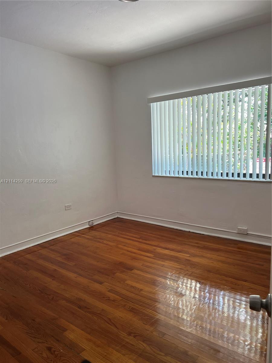 Room featuring wood-finish flooring and a horizontal window with vertical blinds