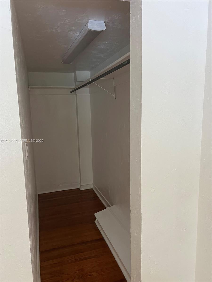 Closet featuring wood-finish flooring, a built-in clothing rod, a white shelf, and a flush-mount ceiling light fixture