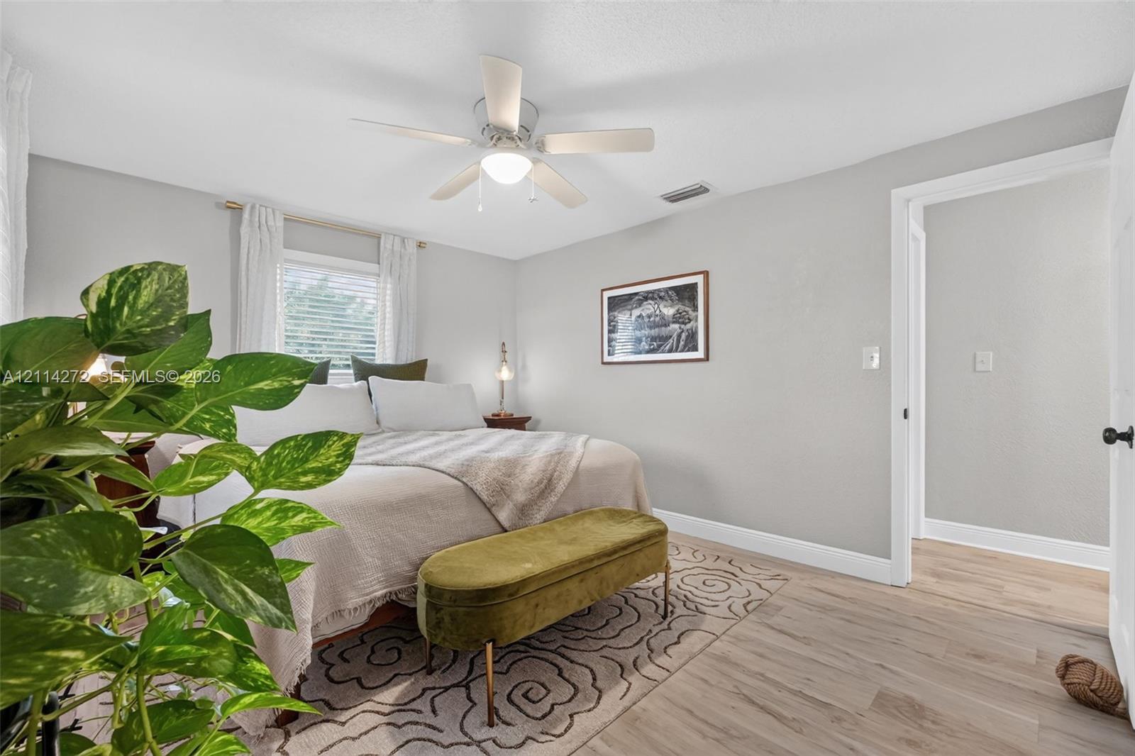 Neutral-toned interior space featuring wood-finish flooring, a white ceiling fan with integrated lighting, and a single-pane window