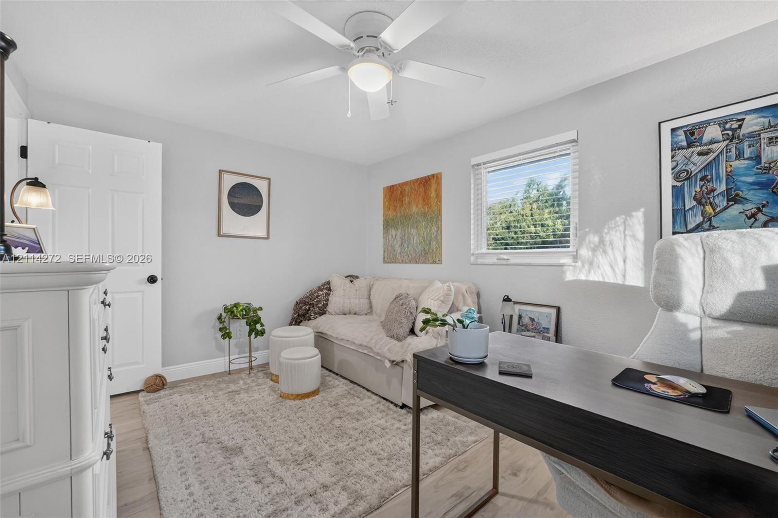 Neutral-toned interior featuring wood-finish flooring, a white ceiling fan with integrated lighting, and a window with horizontal blinds