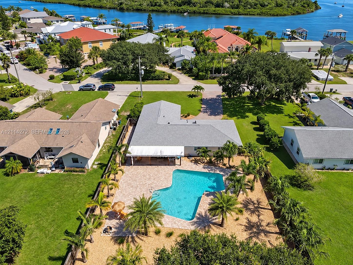 Aerial view of property featuring a rear swimming pool, expansive paver patio, covered lanai, and mature palm trees