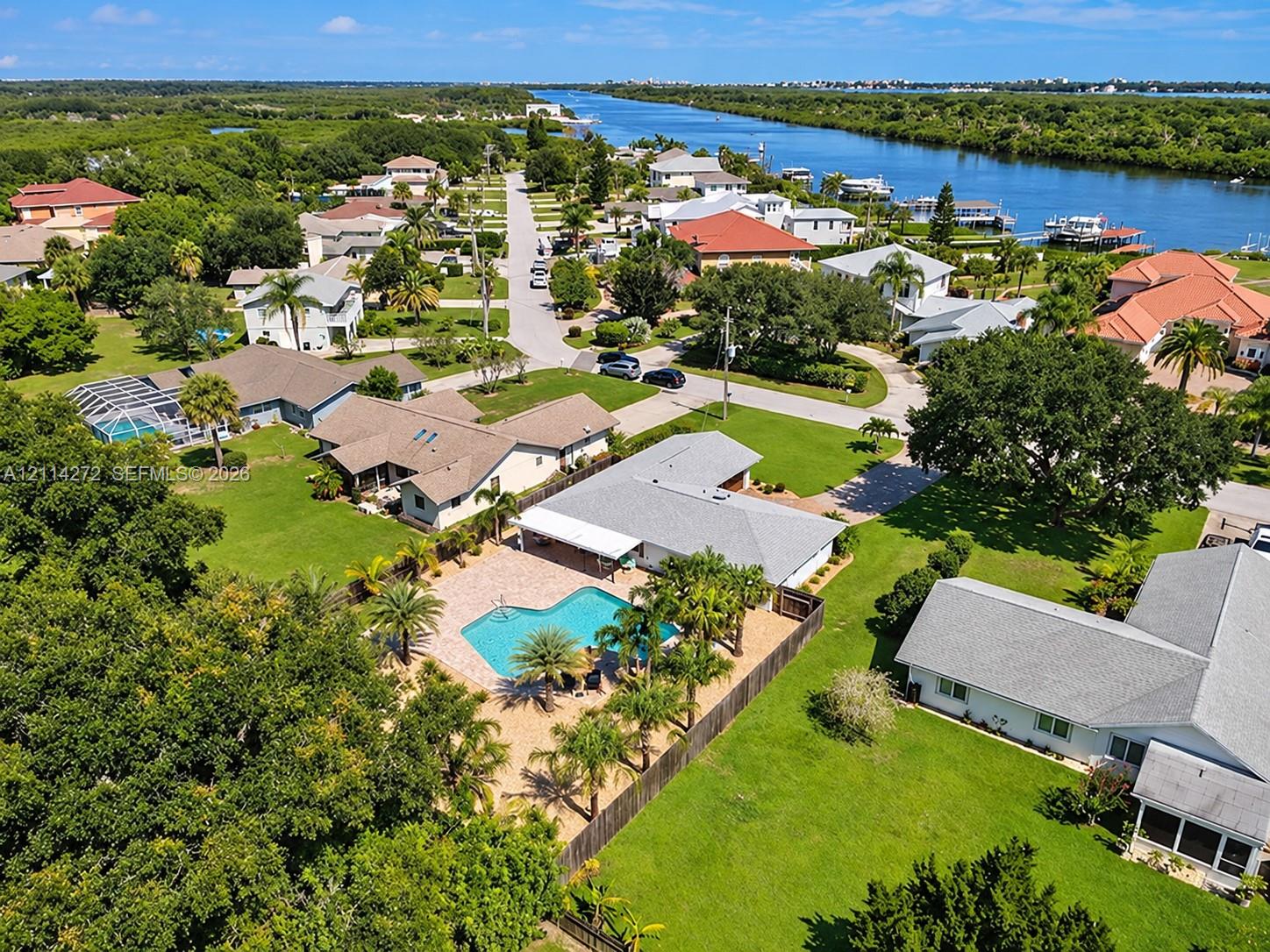 Aerial perspective featuring a single-story residence with a paved pool deck, custom-shaped swimming pool, mature palm trees, and expansive lawn area