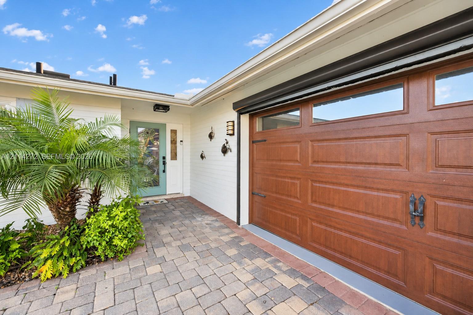 Entryway featuring a paver stone driveway, wood-finish garage door with upper glass panels, and a painted front door with an integrated glass pane