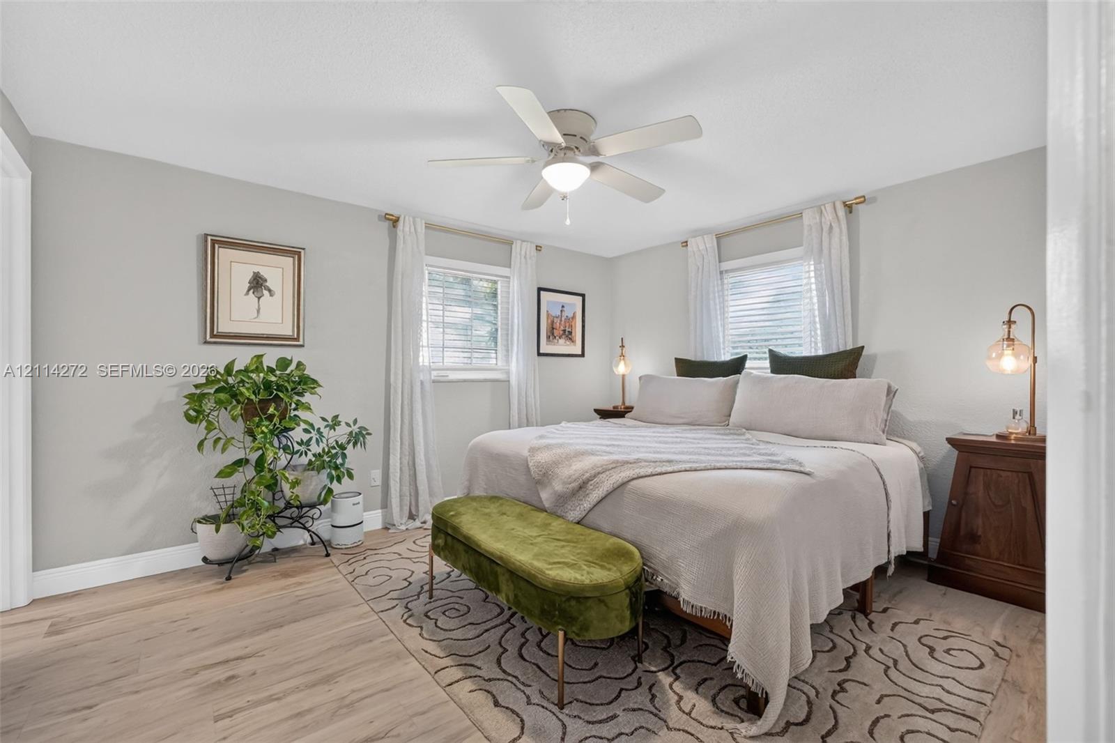 Bedroom featuring wood-finish flooring, a neutral color palette, dual windows with integrated blinds, and a central ceiling fan with an integrated light fixture