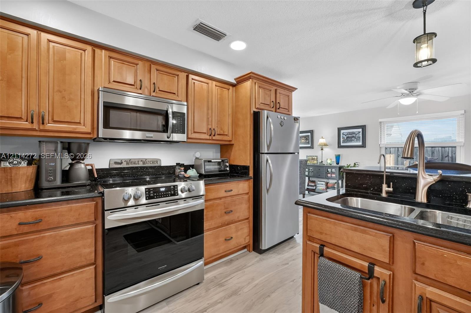 Kitchen featuring natural wood cabinetry, dark stone countertops, stainless steel appliances, a dual-basin undermount sink with a gooseneck faucet, and wood-finish flooring