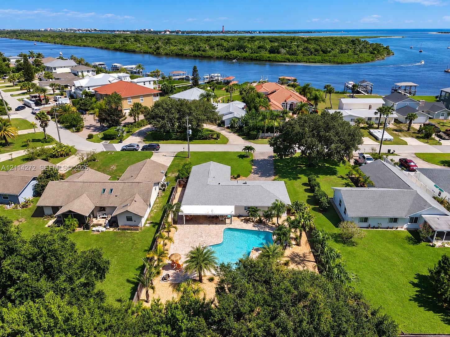 Aerial perspective of a single-story residence featuring a concrete-tile roof, an expansive paved patio, a private in-ground swimming pool, and established landscaping