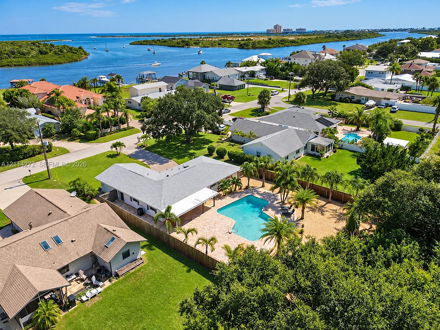 Aerial perspective of a property featuring an in-ground swimming pool, stone-paver pool deck, palm landscaping, and privacy fencing