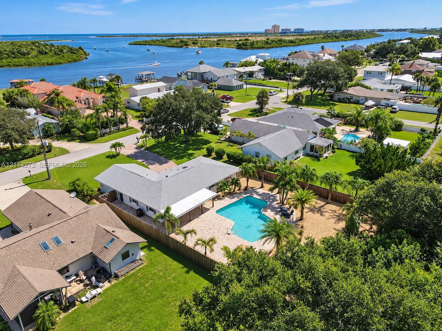 Aerial perspective featuring a detached residence with an in-ground swimming pool, stone-paver pool deck, fenced perimeter, and established landscaping