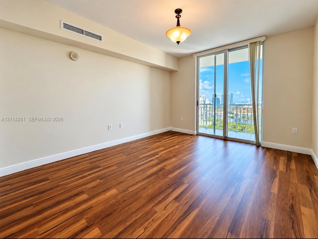 Interior space featuring wood-finish flooring, a ceiling-mounted pendant light fixture, and floor-to-ceiling glass sliding doors providing exterior access