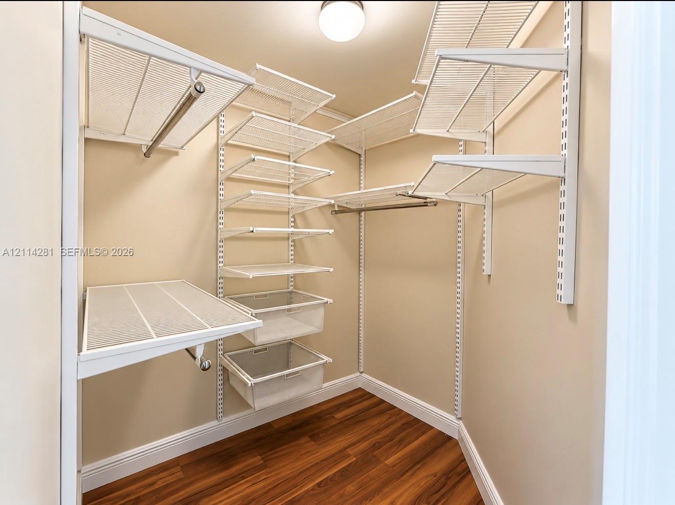 Walk-in storage space featuring wood-finish flooring, adjustable white wire shelving, integrated hanging rods, and pull-out wire baskets