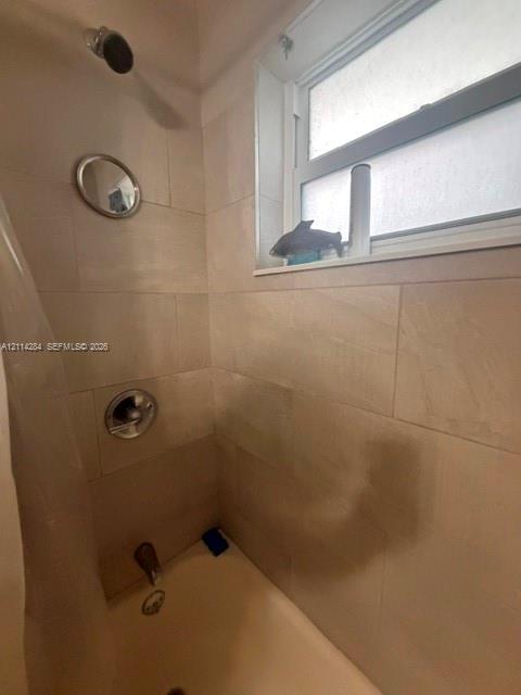 Tub-shower combination featuring large-format neutral wall tile, chrome plumbing fixtures, and an operable window with translucent glass