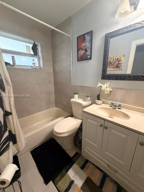 Bathroom featuring a vanity with integrated sink and stone-composite countertop, full-height tile surround in the tub area, and wall-mounted vanity lighting