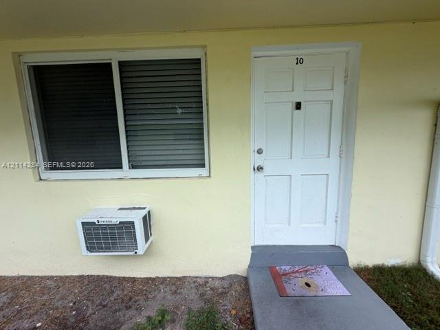 Exterior entry featuring a six-panel door, horizontal sliding window, and wall-mounted air conditioning unit Exterior entry featuring a six-panel door, horizontal sliding window, and wall-mounted air conditioning unit