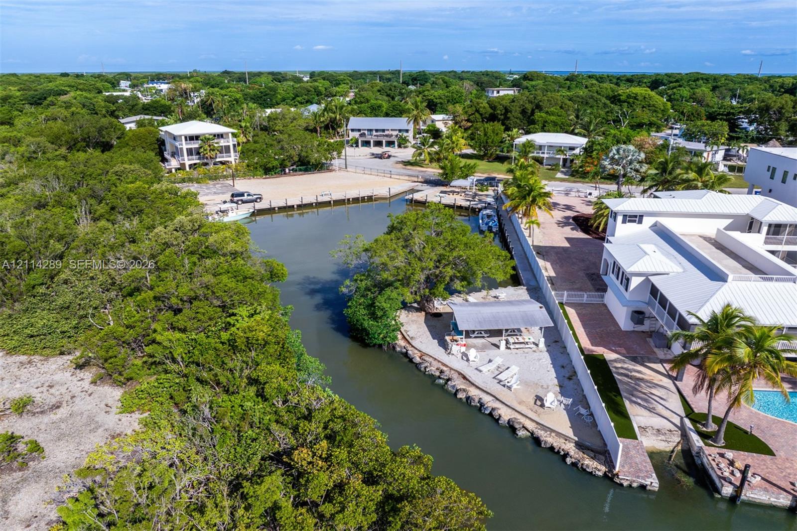 Waterfront property featuring a private boat dock, a covered outdoor pavilion, stone-paver hardscaping, and mature tropical landscaping