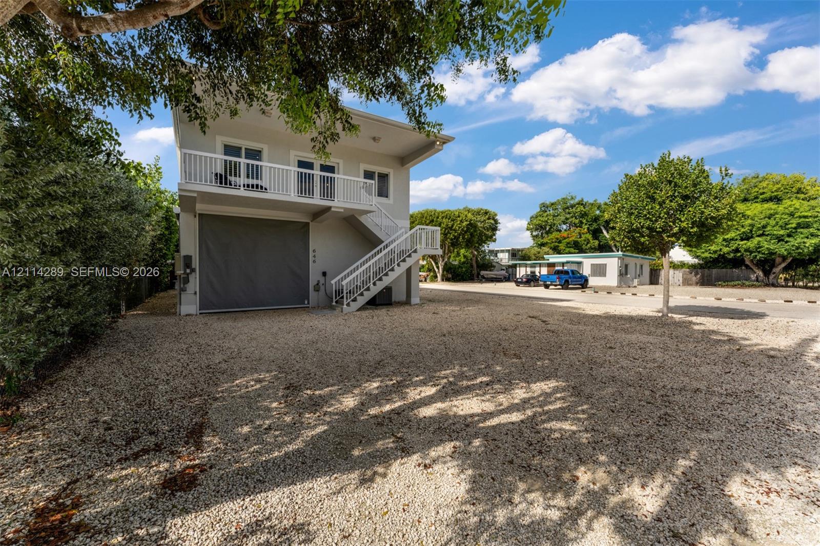 Two-story exterior featuring a gravel driveway, an integrated ground-level garage, and an elevated balcony with white railings and exterior staircase