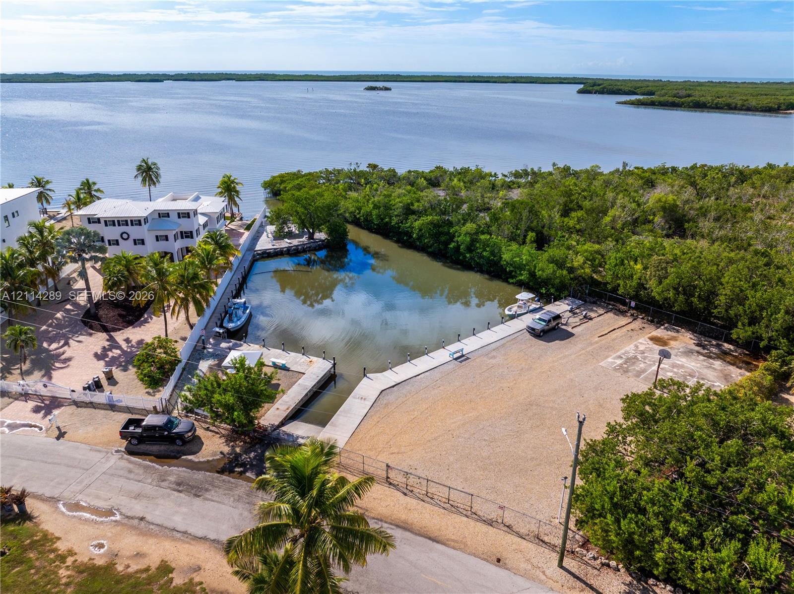 Waterfront lot featuring a concrete boat ramp, deep-water dockage, fenced perimeter, and established tropical landscaping