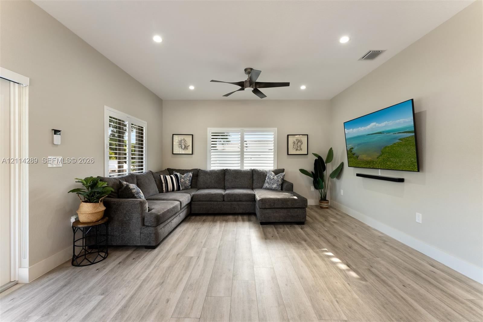 Neutral-toned living space featuring wood-finish flooring, recessed lighting, a modern ceiling fan, and plantation shutters
