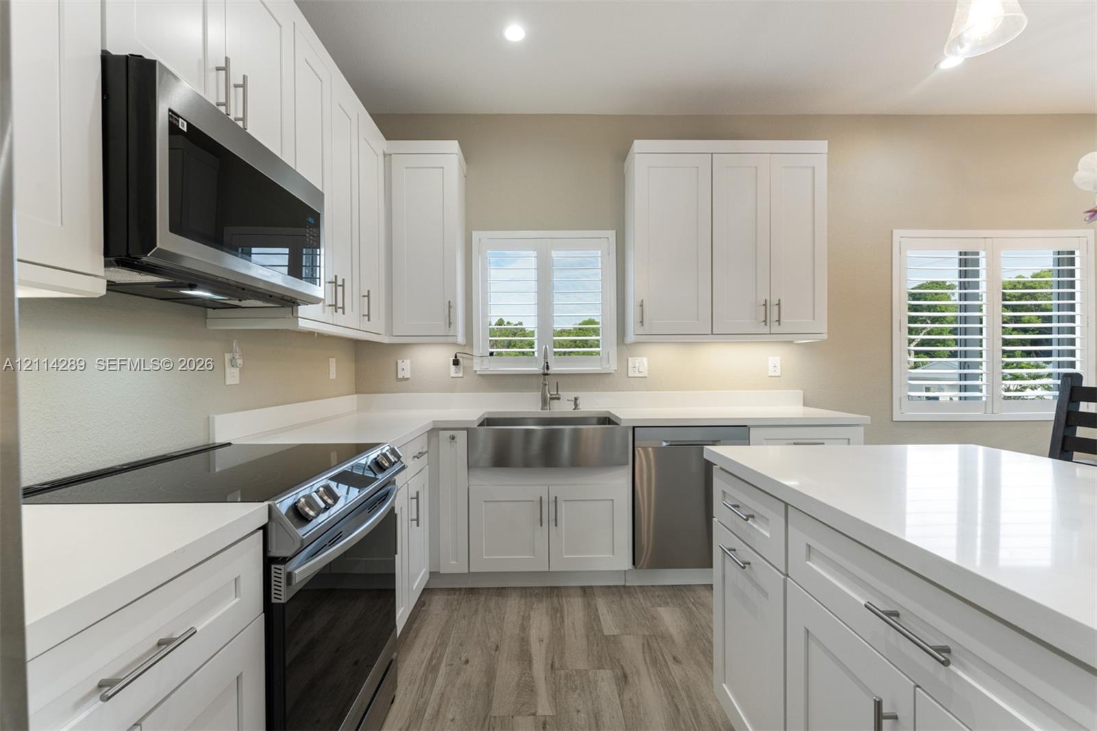Kitchen featuring white shaker-style cabinetry, quartz countertops, a stainless steel apron-front sink, stainless steel appliances, and wood-finish flooring