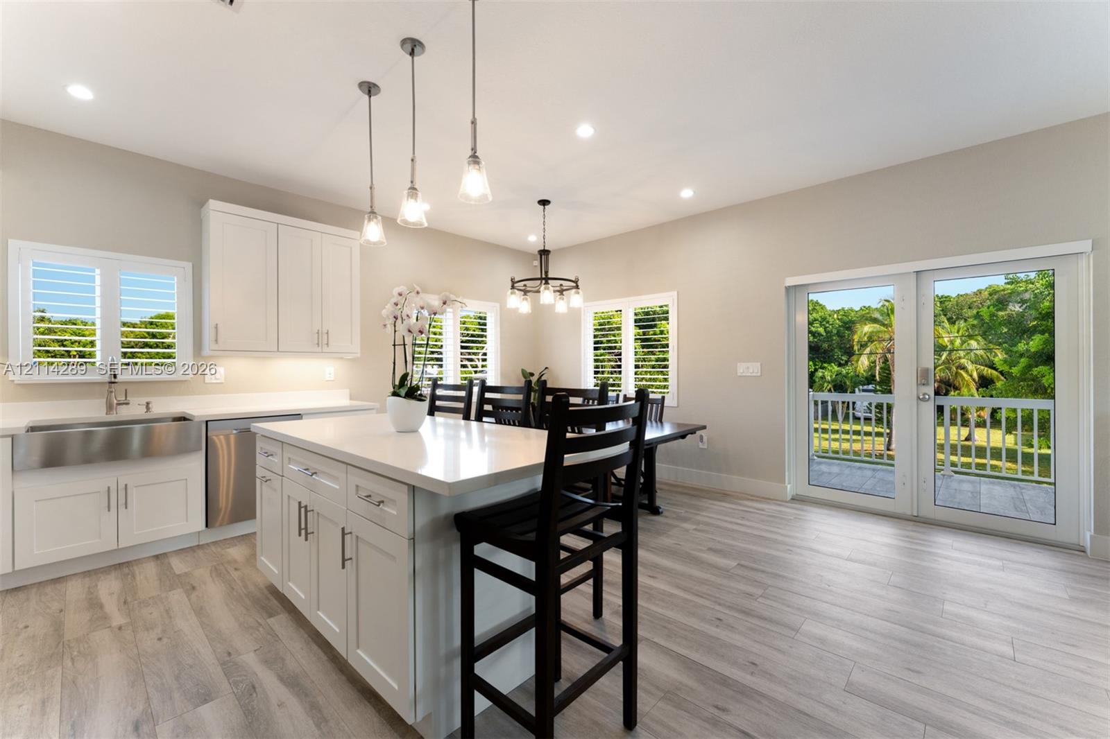 Kitchen featuring white cabinetry, an expansive center island with stone countertop, stainless steel farmhouse sink, wood-finish flooring, and glass-paned double doors with exterior deck access