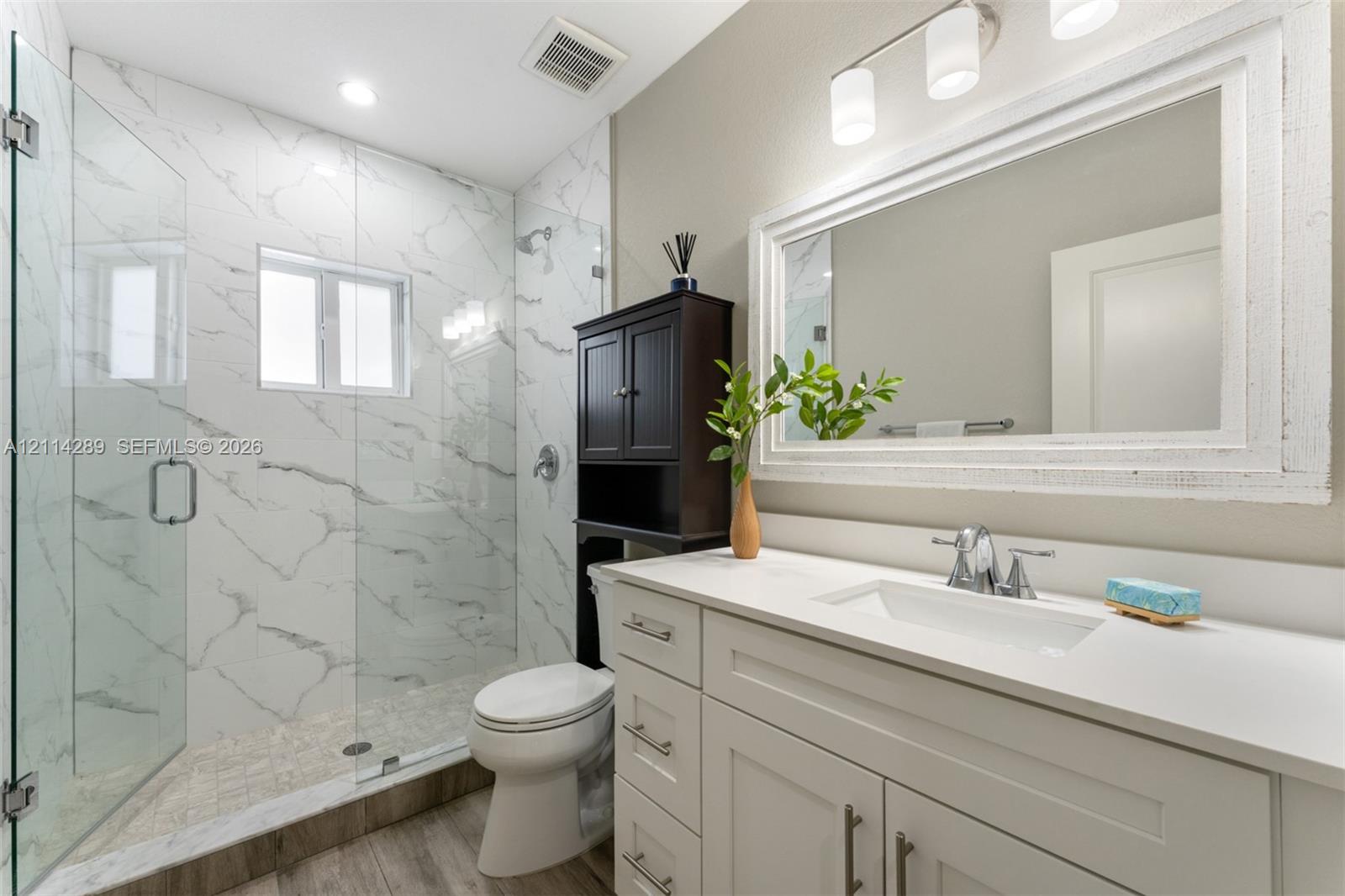 Bathroom featuring a white vanity with a rectangular undermount sink, stone-finish countertop, walk-in shower with floor-to-ceiling tile surround, glass enclosure, and wood-finish flooring
