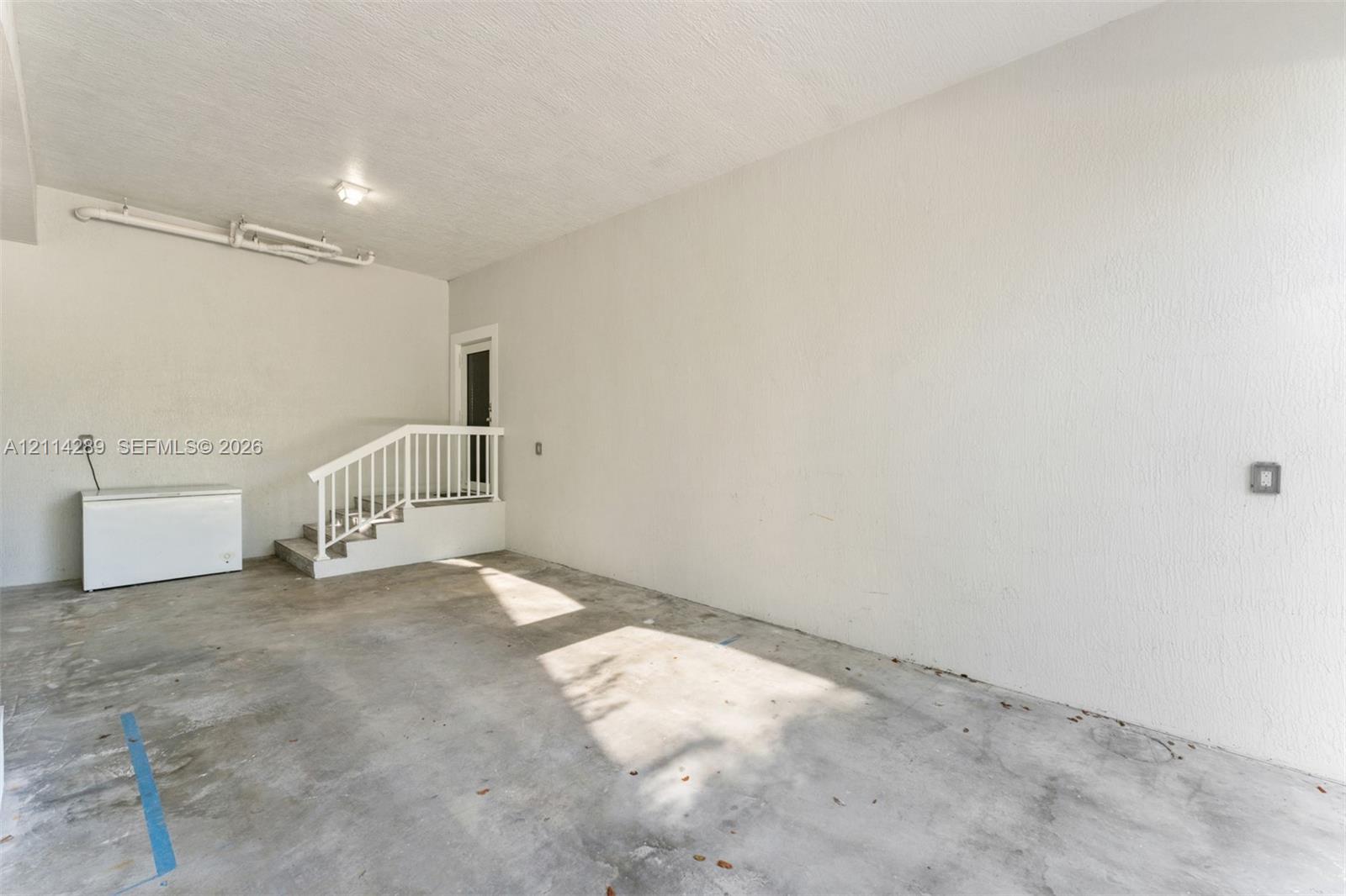 Enclosed garage space featuring a concrete floor, textured walls, and a staircase with a white railing