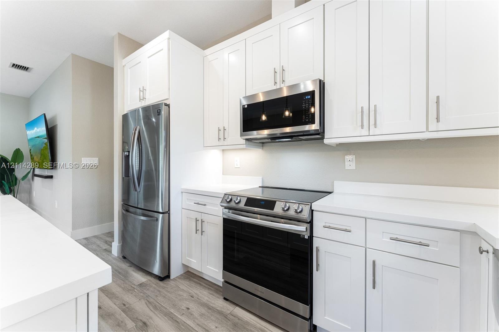 Kitchen featuring white cabinetry, solid-surface countertops, wood-finish flooring, and a stainless steel appliance suite including a built-in microwave and range